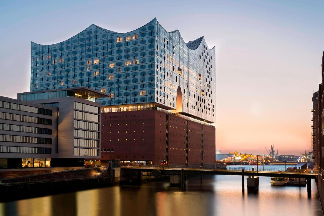 Hotel The Westin Hamburg Elbphilharmonie Exterior foto The photo shows a modern architectural structure located by a body of water, possibly a river or canal. The building features a unique wavy roofline and a facade made of glass and other materials, giving it a contemporary look. It is likely a cultura