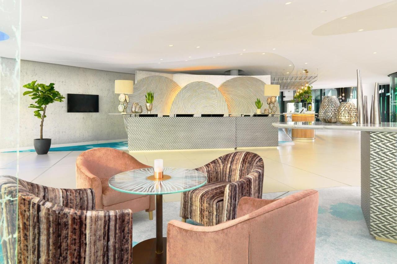 Hotel The Westin Hamburg Elbphilharmonie Exterior foto The photo shows a modern hotel lobby with a stylish reception area. The reception desk has a sleek, contemporary design and is centered against a light-colored wall featuring abstract patterns. 

In front of the desk, there are two sets of seating ar