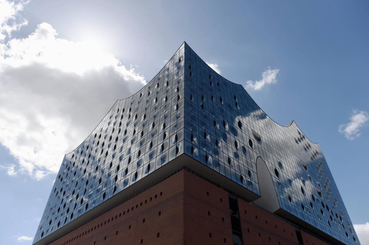 Hotel The Westin Hamburg Elbphilharmonie Exterior foto The photo shows a modern architectural building characterized by a distinctive, wavy glass facade. The structure has a bluish tint with many large windows that reflect the sky and surrounding environment. The lower section of the building is made of 