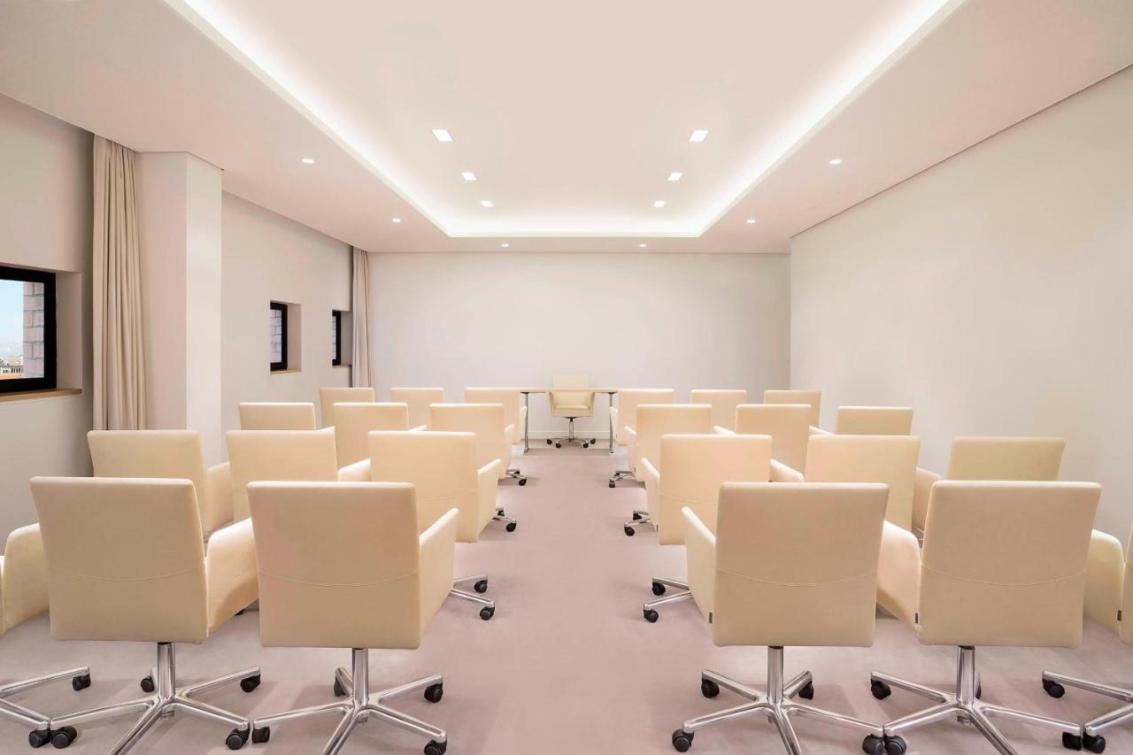 Hotel The Westin Hamburg Elbphilharmonie Exterior foto The photo shows a modern conference room. There are several light-colored, wheeled chairs arranged in rows facing a central area where a glass table is located. The room has soft lighting from recessed ceiling lights, and the walls are mostly white, 