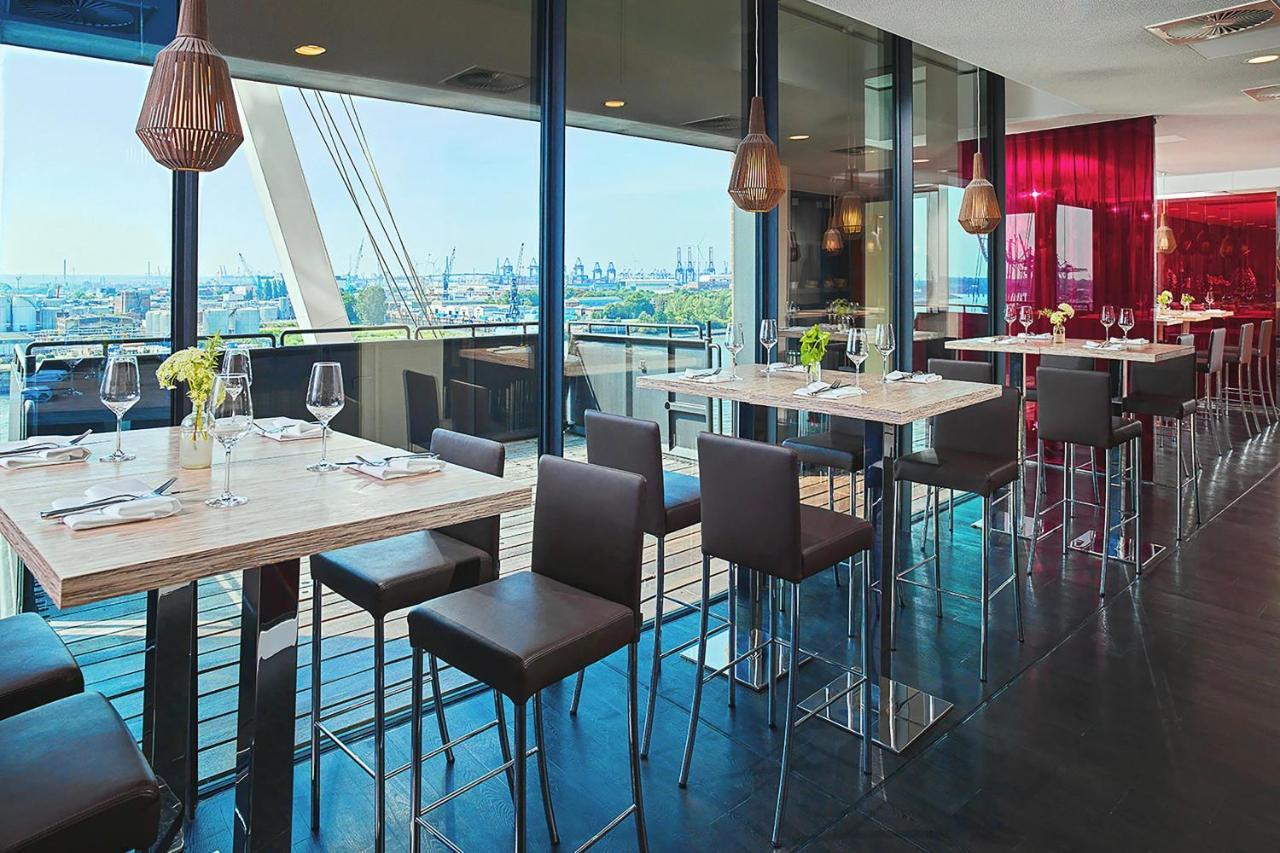 Hotel The Westin Hamburg Elbphilharmonie Exterior foto The photo depicts a modern restaurant interior featuring a spacious dining area with large windows that provide a view of the outside. There are several tall tables with a light-colored surface and metallic bases, accompanied by dark, sleek stools. T