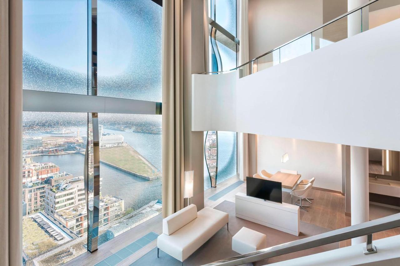 Hotel The Westin Hamburg Elbphilharmonie Exterior foto The photo showcases a modern, stylish interior of a multi-level living space. It features large, floor-to-ceiling windows that provide a panoramic view of the surrounding landscape and water. The decor is minimalist, with a predominantly white color 