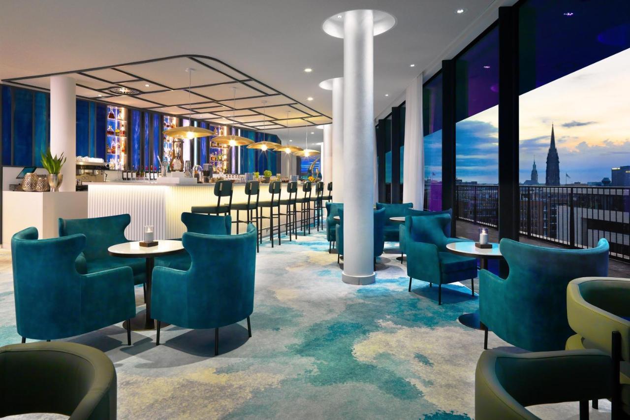 Hotel The Westin Hamburg Elbphilharmonie Exterior foto The photo shows a modern lounge or bar area with a stylish design. It features plush turquoise chairs and small tables arranged around the space. In the background, there's a long bar with seating, illuminated by soft lighting. Large windows provide 