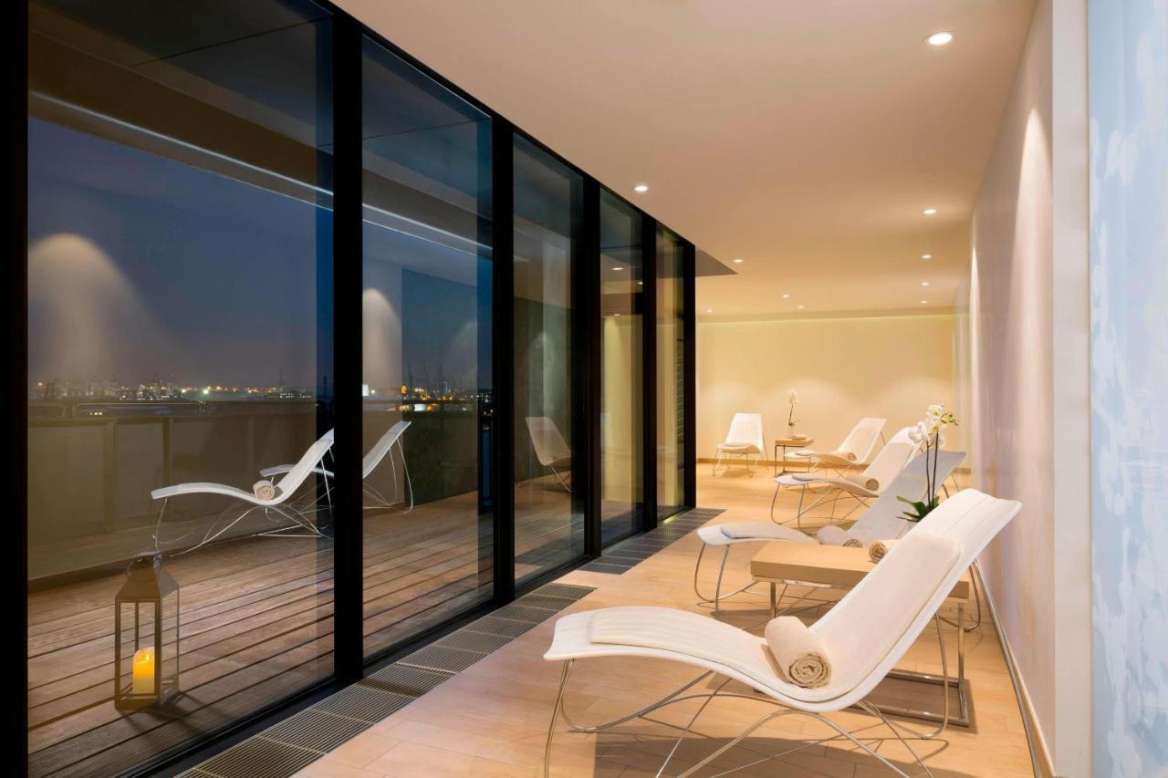 Hotel The Westin Hamburg Elbphilharmonie Exterior foto The photo shows a modern, stylish indoor space with large glass windows that offer a view of the night. The area is illuminated softly, highlighting a sleek and minimalist design. There are several white lounge chairs arranged on a wooden deck, creat