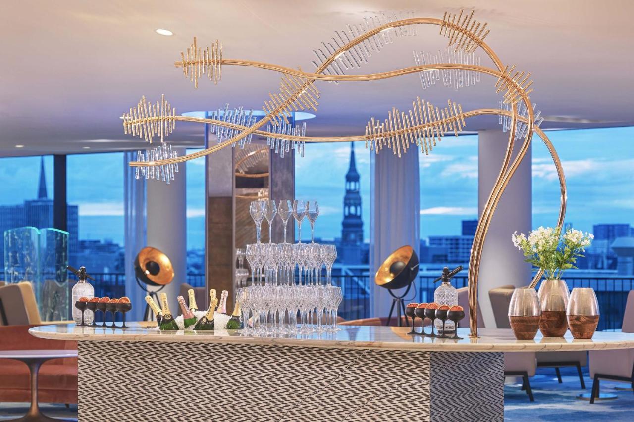 Hotel The Westin Hamburg Elbphilharmonie Exterior foto The photo depicts a stylish bar setup in a modern venue. The bar features an elegant design with a patterned front and a sleek countertop. Above the bar, there is a striking decorative element that resembles a stylized tree or wave, made from metalli