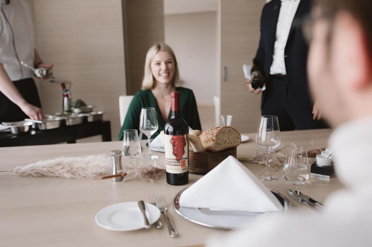 Hotel The Westin Hamburg Elbphilharmonie Exterior foto The image shows a dining setting with a woman smiling at the table. She is seated in front of a bottle of red wine that has a distinctive label. There is also bread and a neatly arranged table setting, including plates and glasses. In the background,