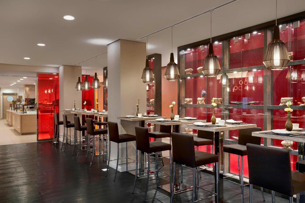 Hotel The Westin Hamburg Elbphilharmonie Exterior foto The photo shows a modern restaurant interior featuring a sleek, contemporary design. There are high tables with bar stools arranged along one side, illuminated by stylish hanging pendant lights. The color scheme includes warm tones, with red accents 