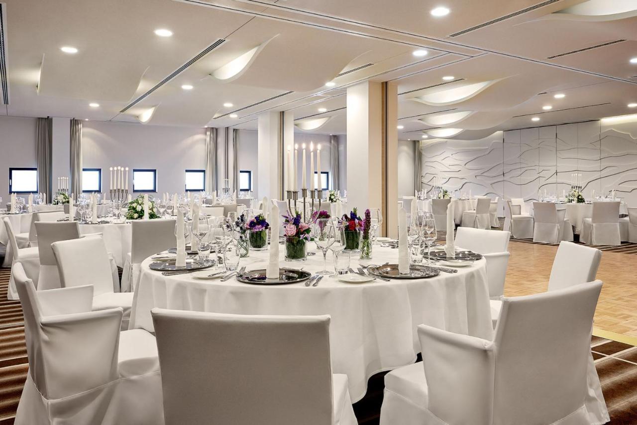 Hotel The Westin Hamburg Elbphilharmonie Exterior foto The photo depicts a modern banquet or event hall setup. It features round tables covered with white tablecloths, each set with elegant dishware and glassware. The tables are adorned with floral centerpieces, adding a touch of color, and there are tal