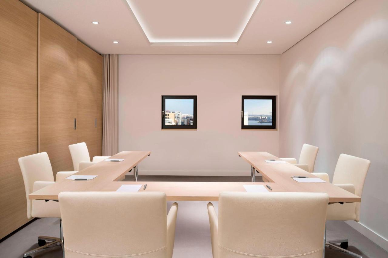 Hotel The Westin Hamburg Elbphilharmonie Exterior foto The photo shows a modern conference room. It features a long, rectangular table made of light-colored wood, surrounded by several cream-colored chairs. The walls are painted in a light shade, and there are two framed windows on one wall that provide 