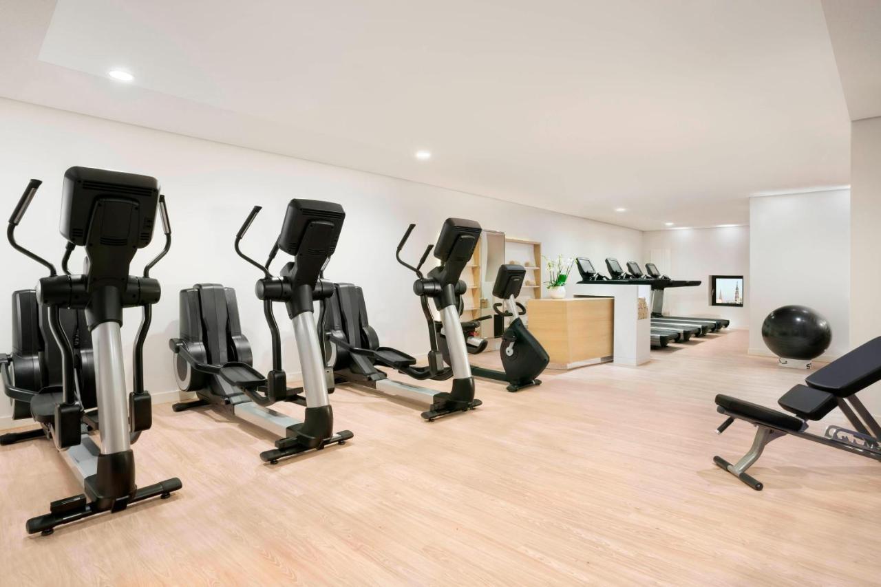 Hotel The Westin Hamburg Elbphilharmonie Exterior foto The photo shows a fitness room with several pieces of exercise equipment. On the left side, there are multiple elliptical machines arranged in a row. In the center, there is a stationary bike. A workout bench is positioned nearby, and a large exercis