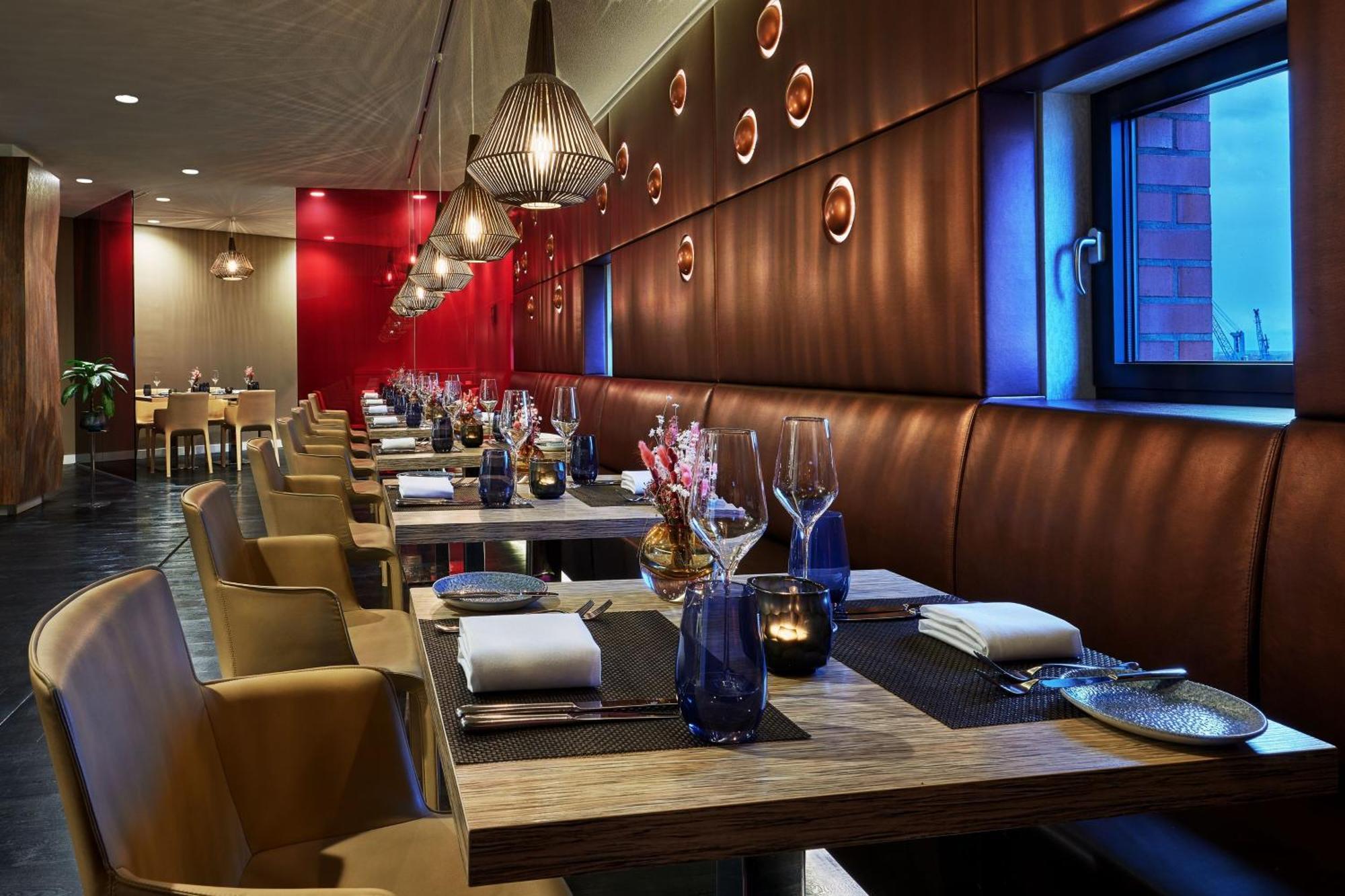 Hotel The Westin Hamburg Elbphilharmonie Exterior foto The photo shows a modern restaurant interior. It features a series of wooden tables set for dining, each equipped with white napkins and utensils. The seating consists of comfortable leather chairs. The walls are decorated with a combination of warm 