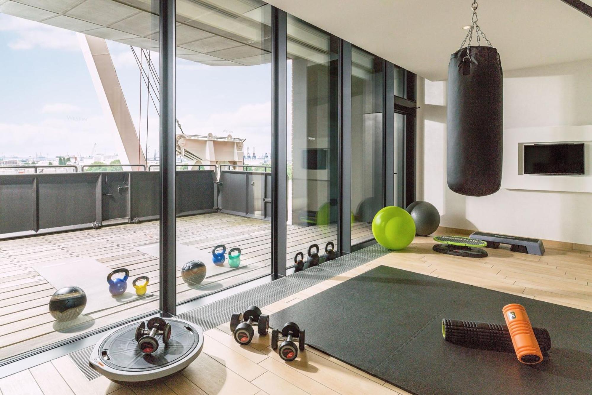 Hotel The Westin Hamburg Elbphilharmonie Exterior foto The photo shows a modern home gym with large glass windows that provide a view to the outside. Inside, there are various fitness equipment items, including a heavy punching bag hanging from the ceiling, kettlebells, a stability ball, an exercise mat,
